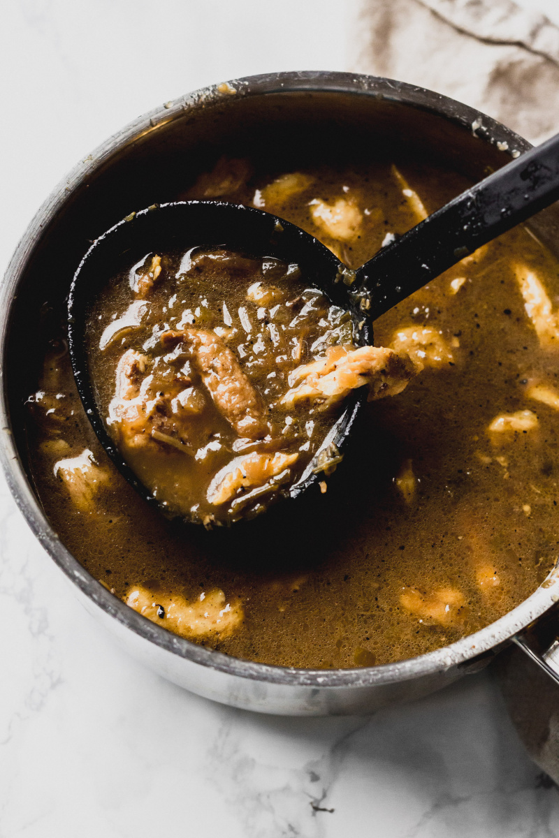 close up of a ladel in a pot of gumbo with chicken and sausage