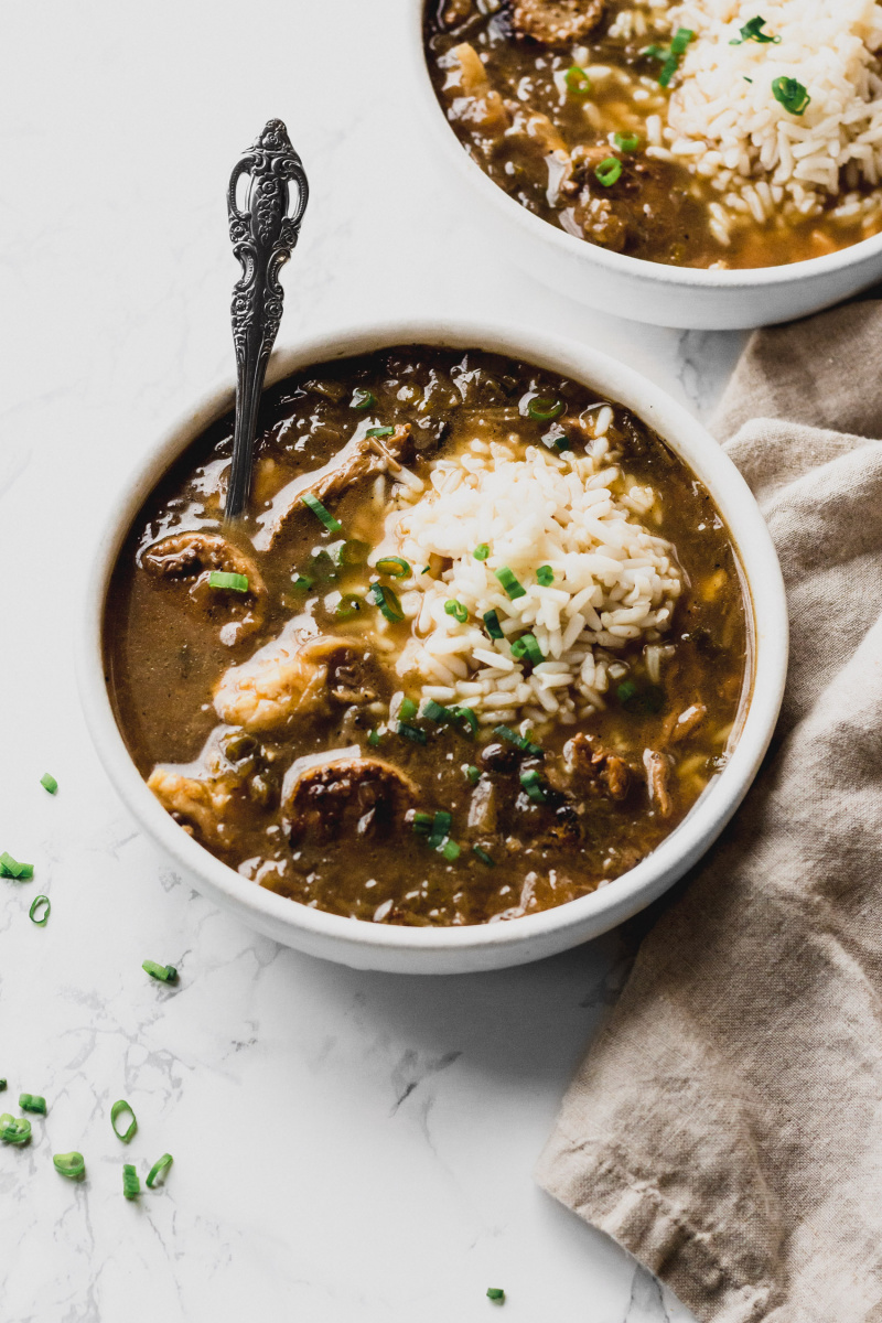 side view of a bowl of thin brown gumbo with a spoon