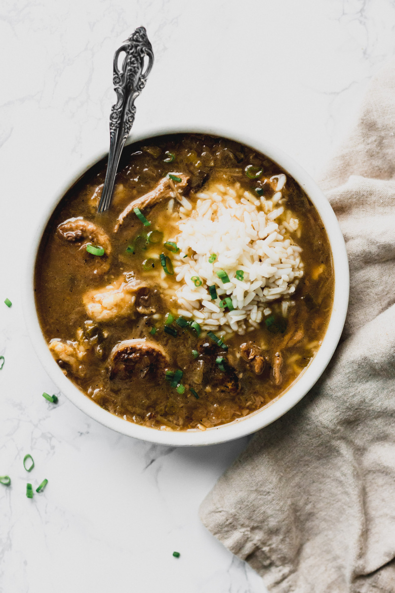 overhead view of a bowl of brown gumbo with a scoop of rice and chopped green onions on top