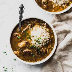 white bowl of thin brown gumbo with rice and green onions