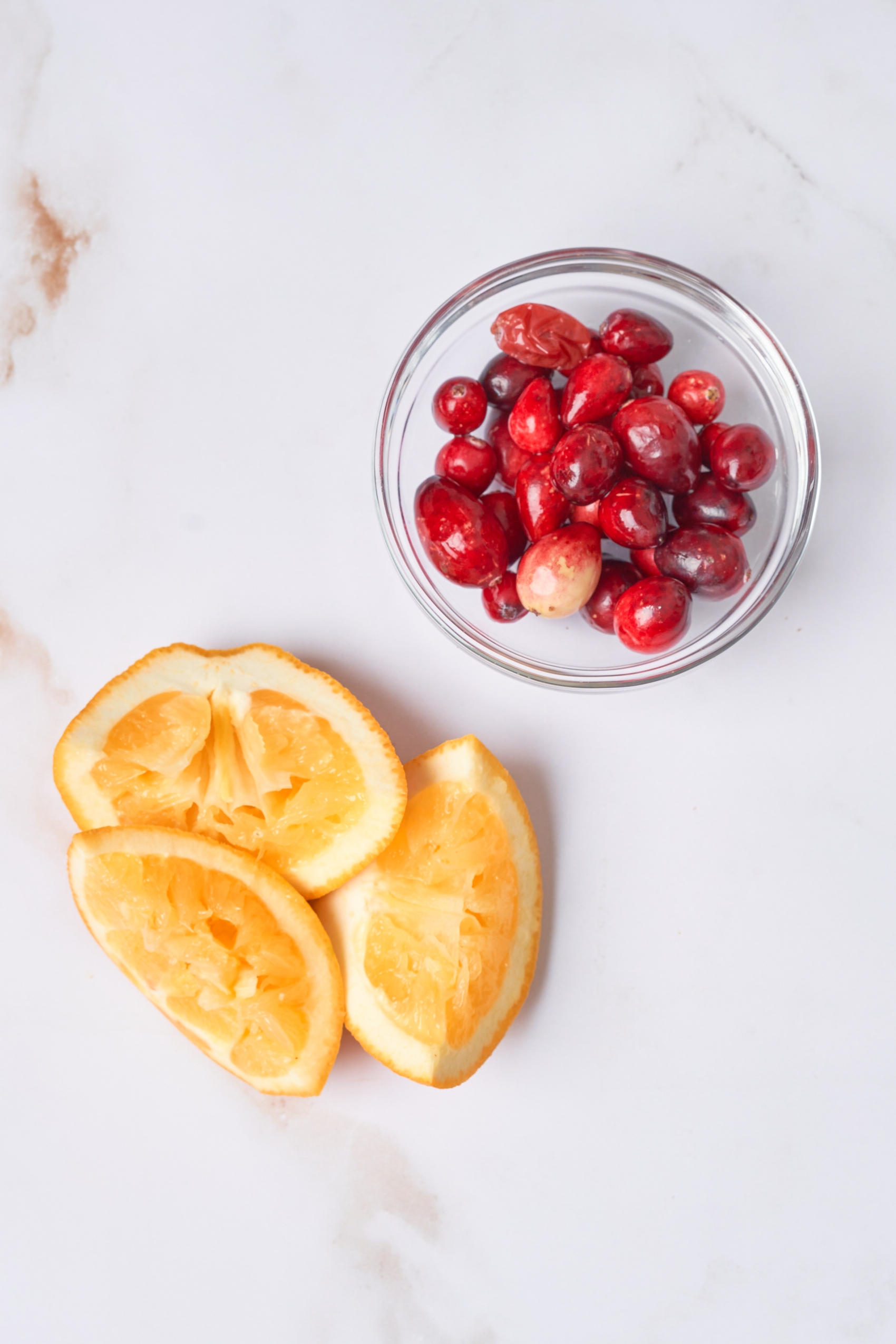 three slices of squeezed oranges and a bowl of fresh cranberries