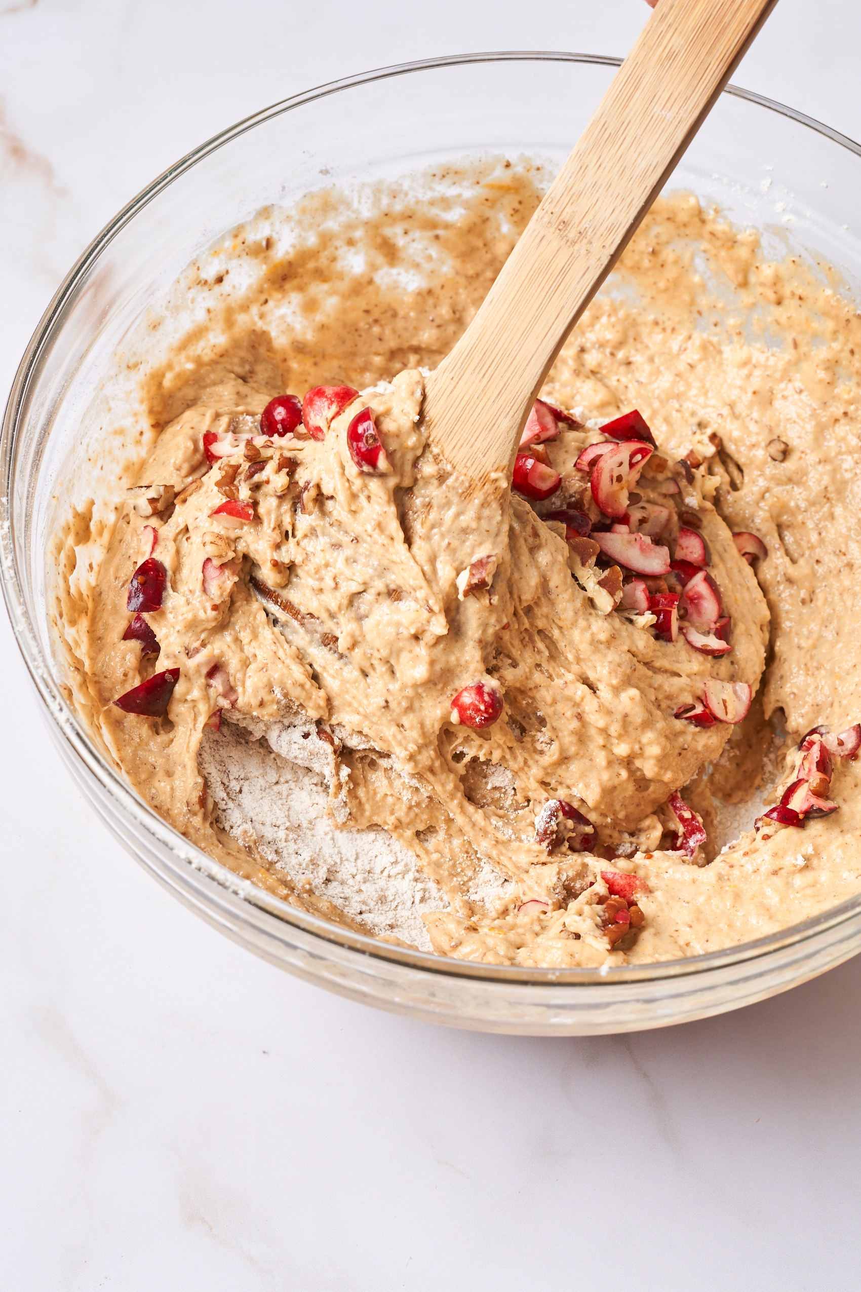 a wooden spoon stirring cranberries into a bread batter