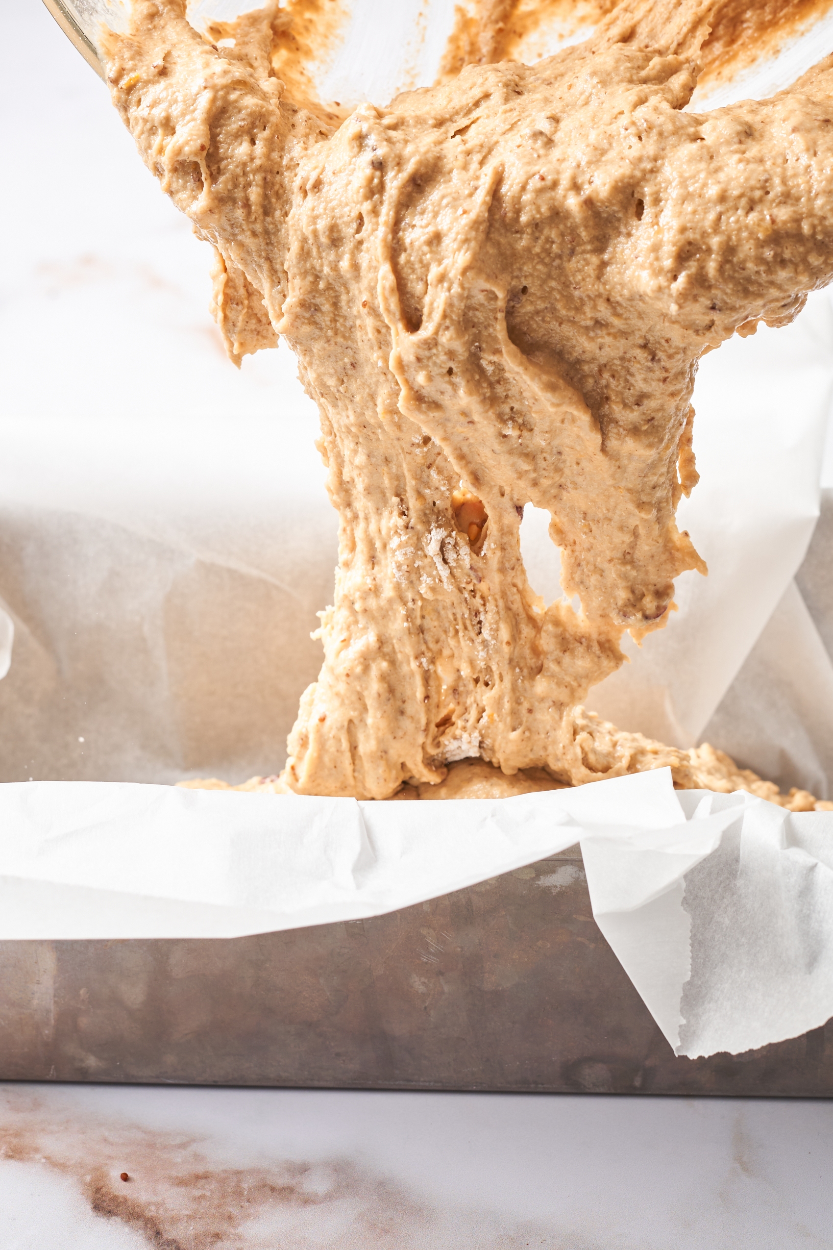 bread batter being poured into a bread pan lined with parchment paper