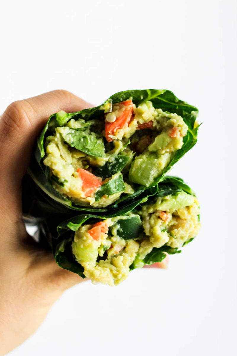 An avocado chickpea salad served in a collard wrap. A hand holds both halves of the wrap showcasing the filling