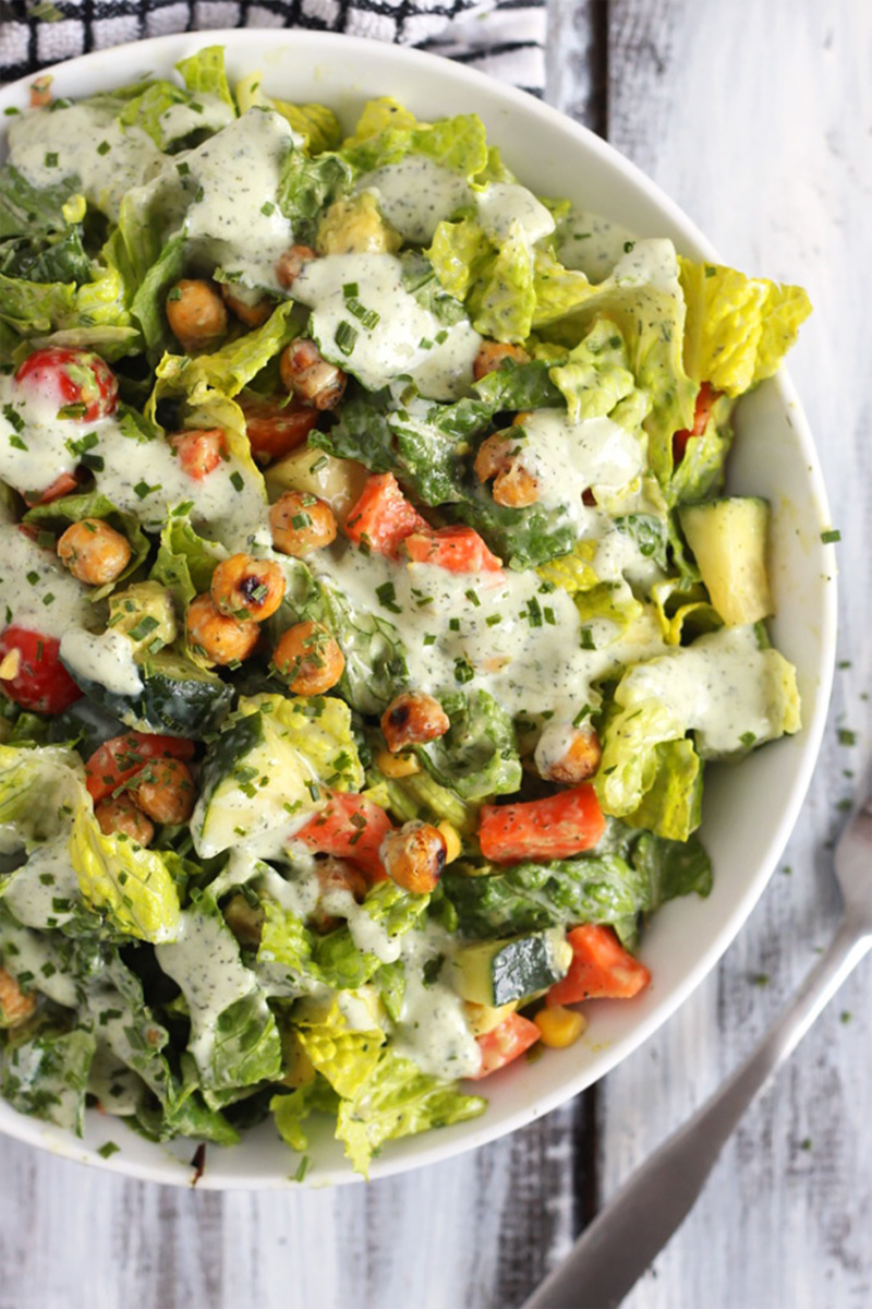 A romaine salad topped with red bell peppers, chives, and vegan ranch dressing