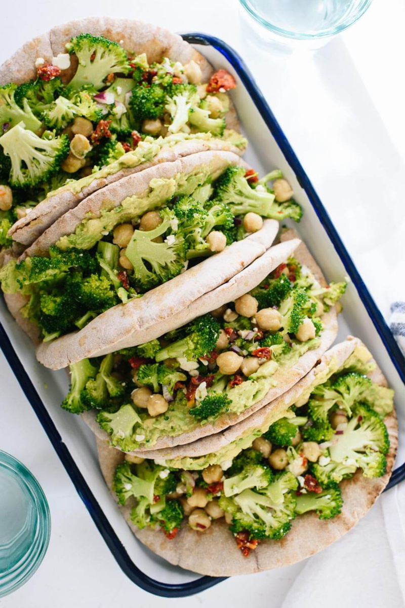 Four pita sandwiches filled with broccoli, avocado and chickpeas, served in a white dish