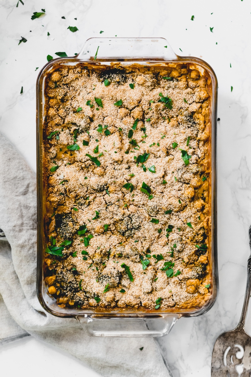 A glass casserole dish on a white countertop containing a cheesy chickpea casserole