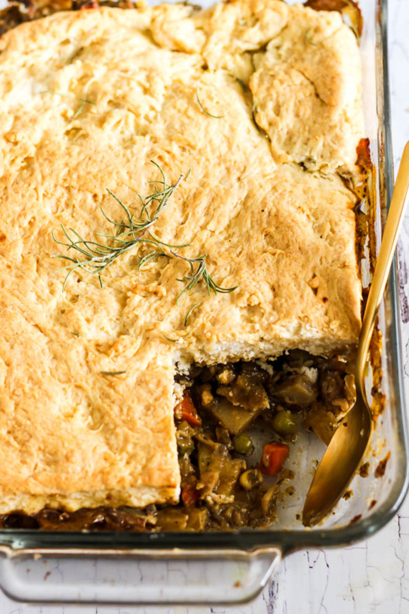 A chickpea pot pie served in a casserole dish. One scoop has been served from the pot pie, revealing the vegetable filling