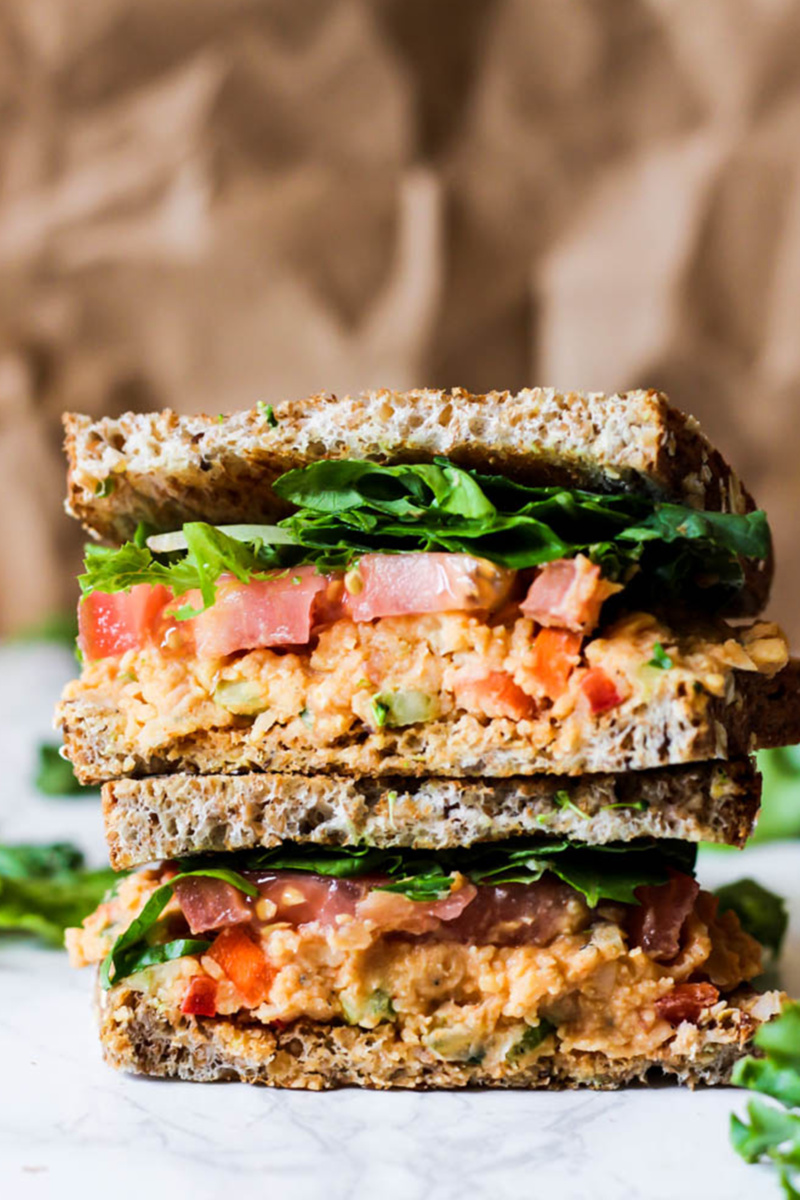 Two halves of a buffalo chickpea sandwich stacked on top of one another. The sandwich is topped with lettuce and tomato