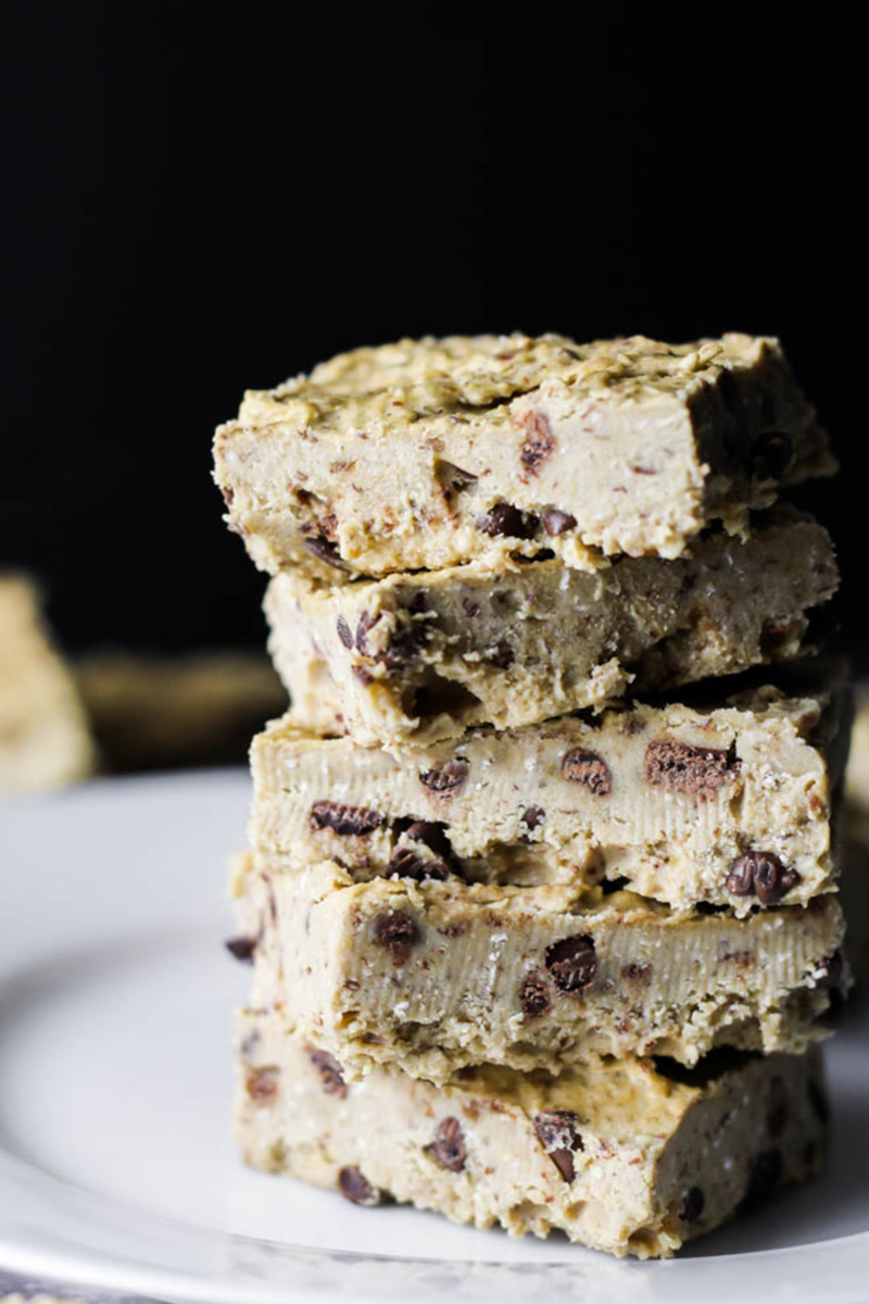 5 pieces of vegan chickpea cookie dough fudge stacked on top of a white plate against a black background