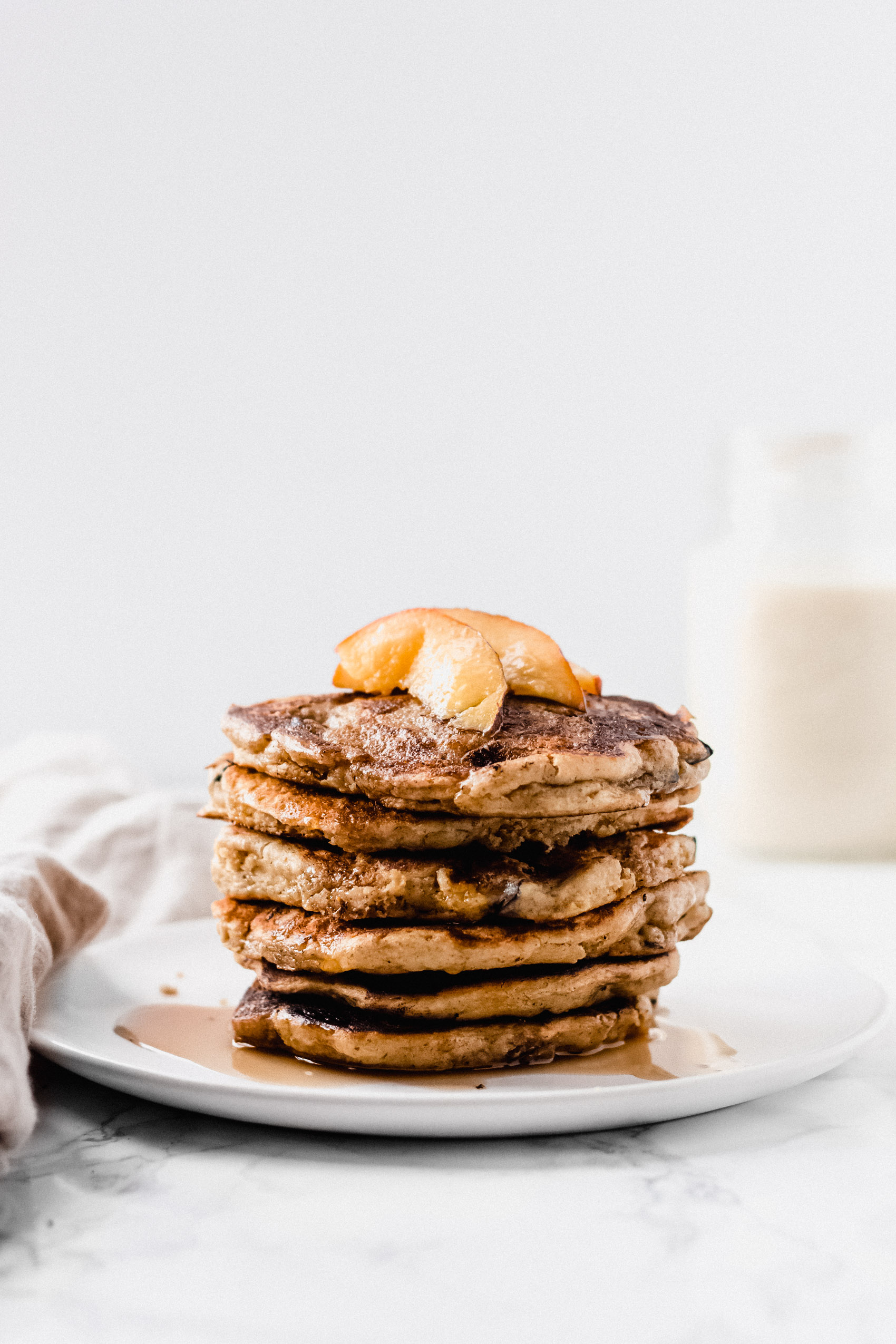 a stack of pancakes with sliced peaches and maple syrup on top