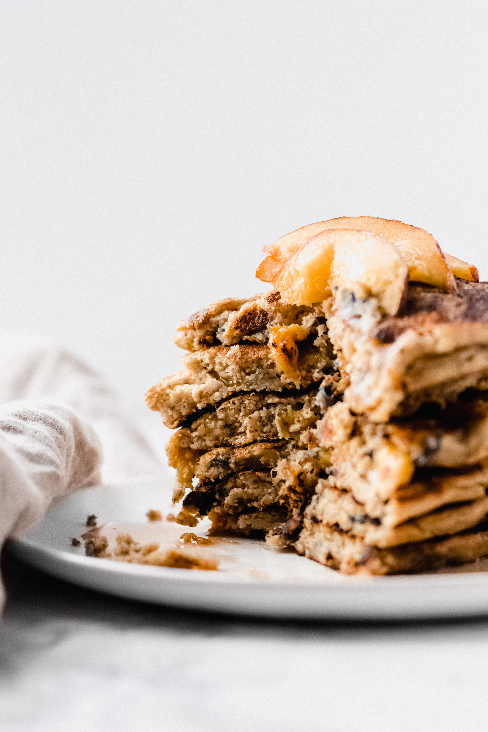 five pancakes stacked with peaches and maple syrup with a slice taken out