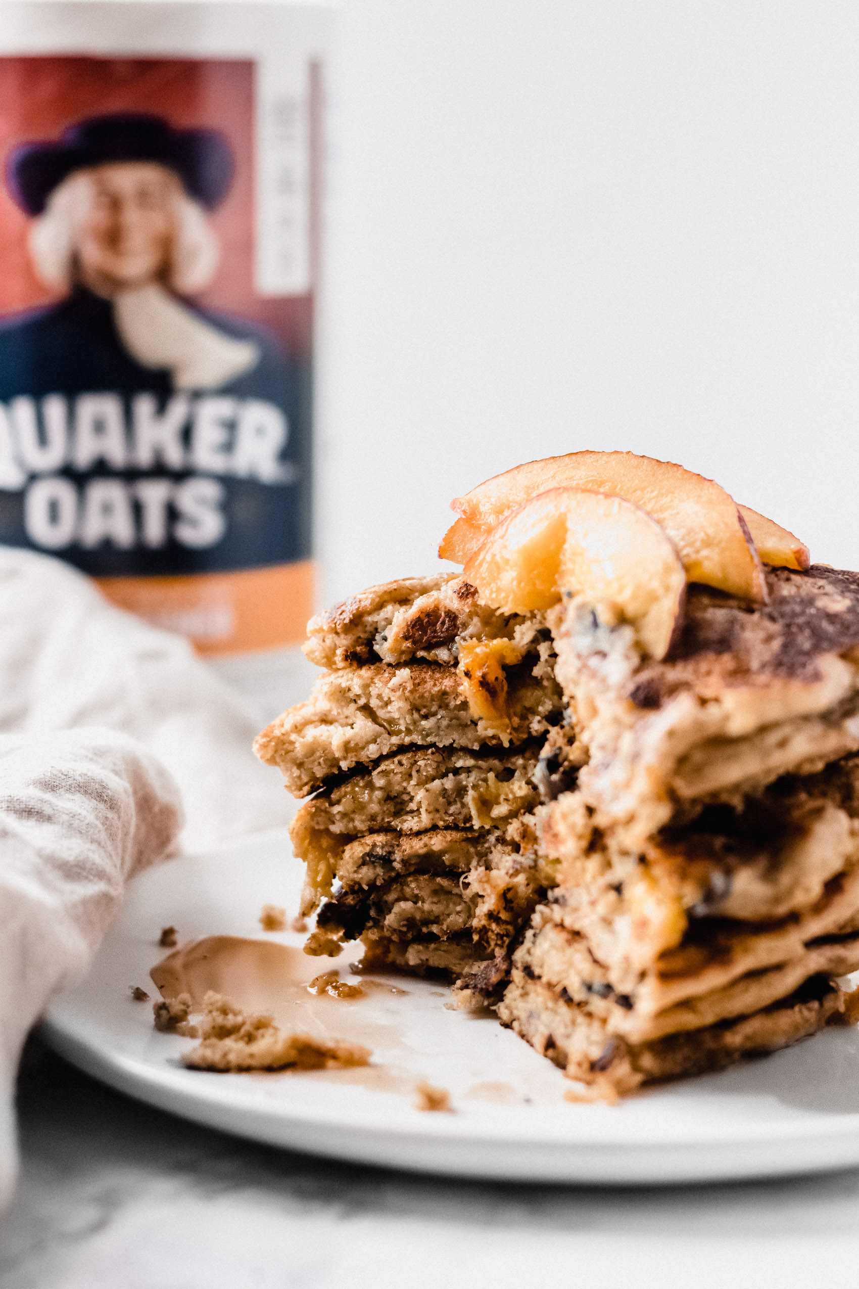 a stack of pancakes with a slice taken out and a carton of oats behind them