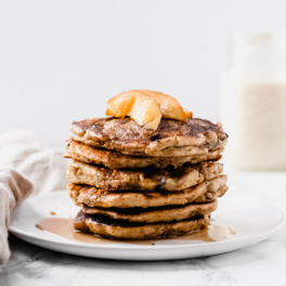 a stack of pancakes with sliced peaches and maple syrup on top