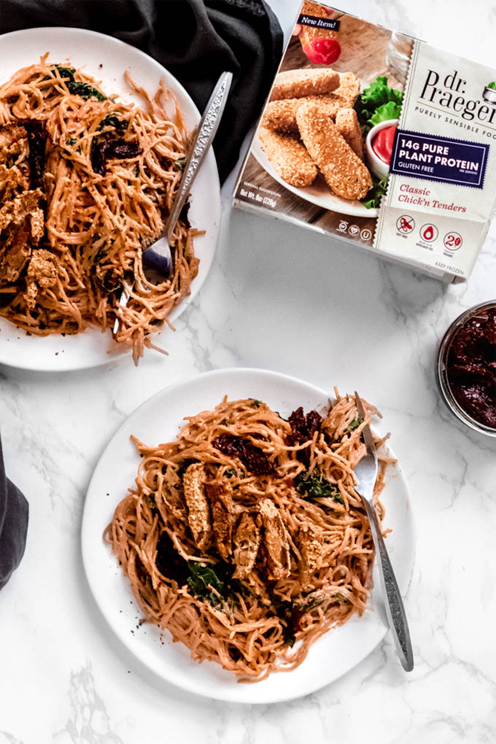 a box of vegan chicken tenders next to two plates of sun dried tomato pasta