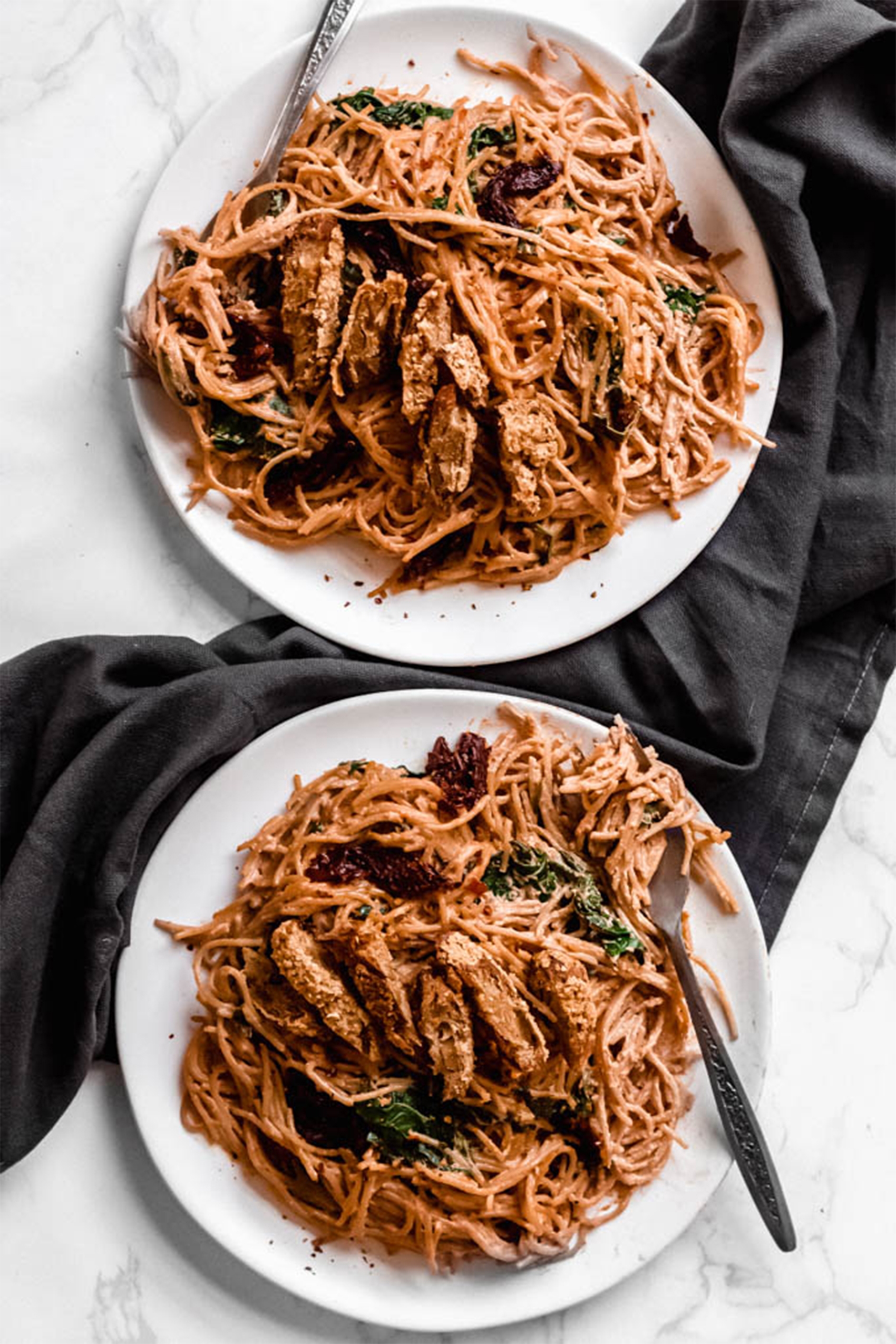 two plates of sundried tomato pasta with vegan chicken strips