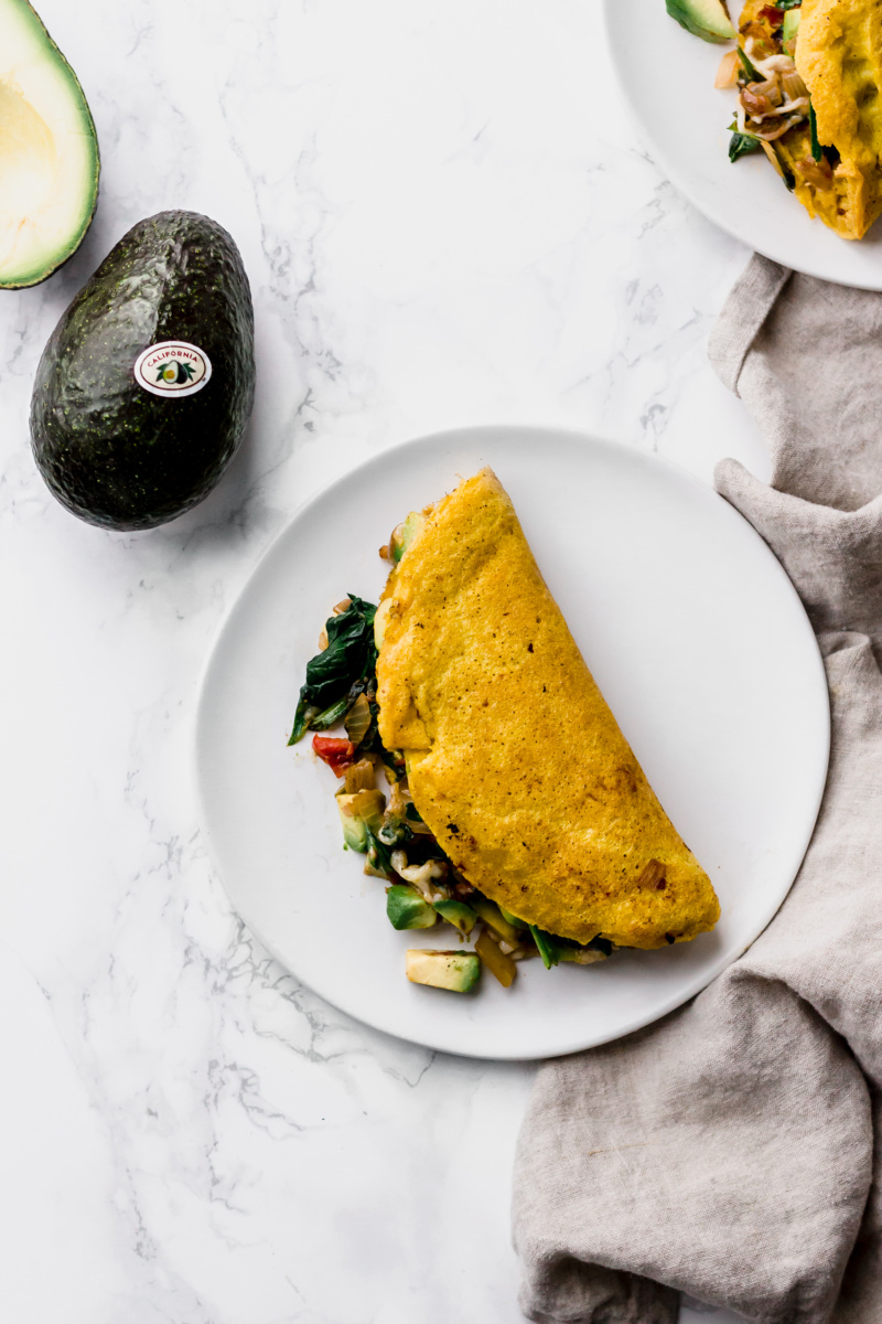 omelette stuffed with vegetables with a whole avocado on the side