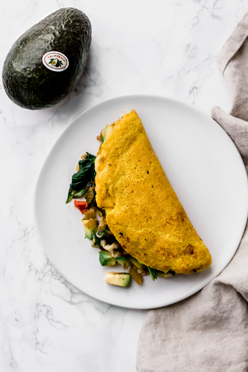 close up of an omelette stuffed with vegetables with a whole avocado on the side