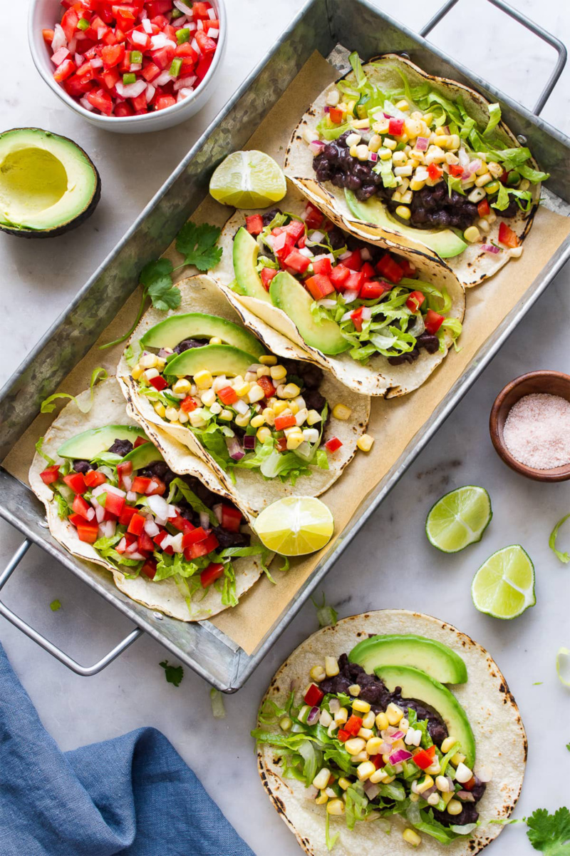 a tray of corn and black bean tacos served with limes