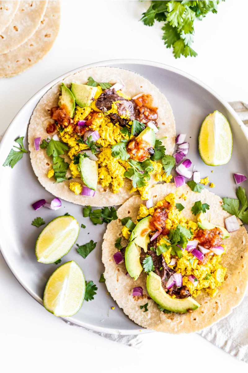 a plate of two vegan breakfast tacos served with limes