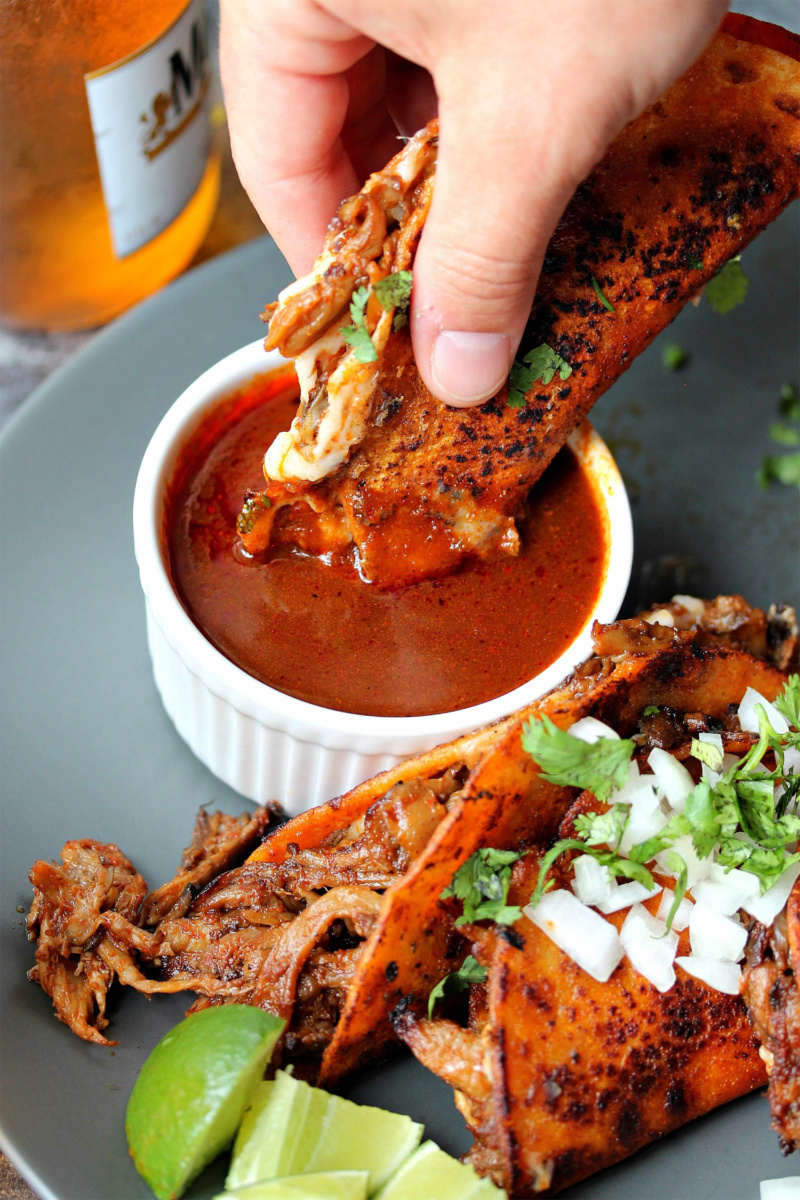 vegan birria tacos being dipped into consume