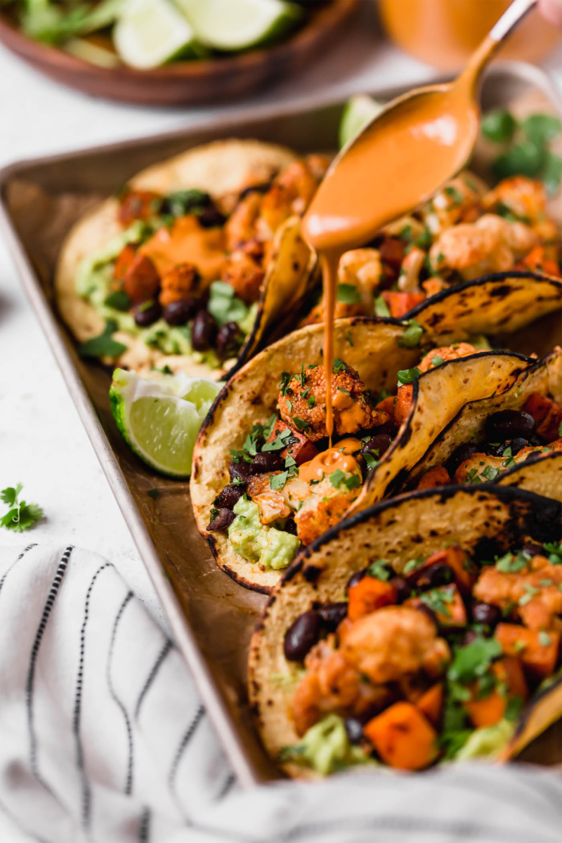 a sheet tray of roasted cauliflower tacos being drizzled with cashew sauce