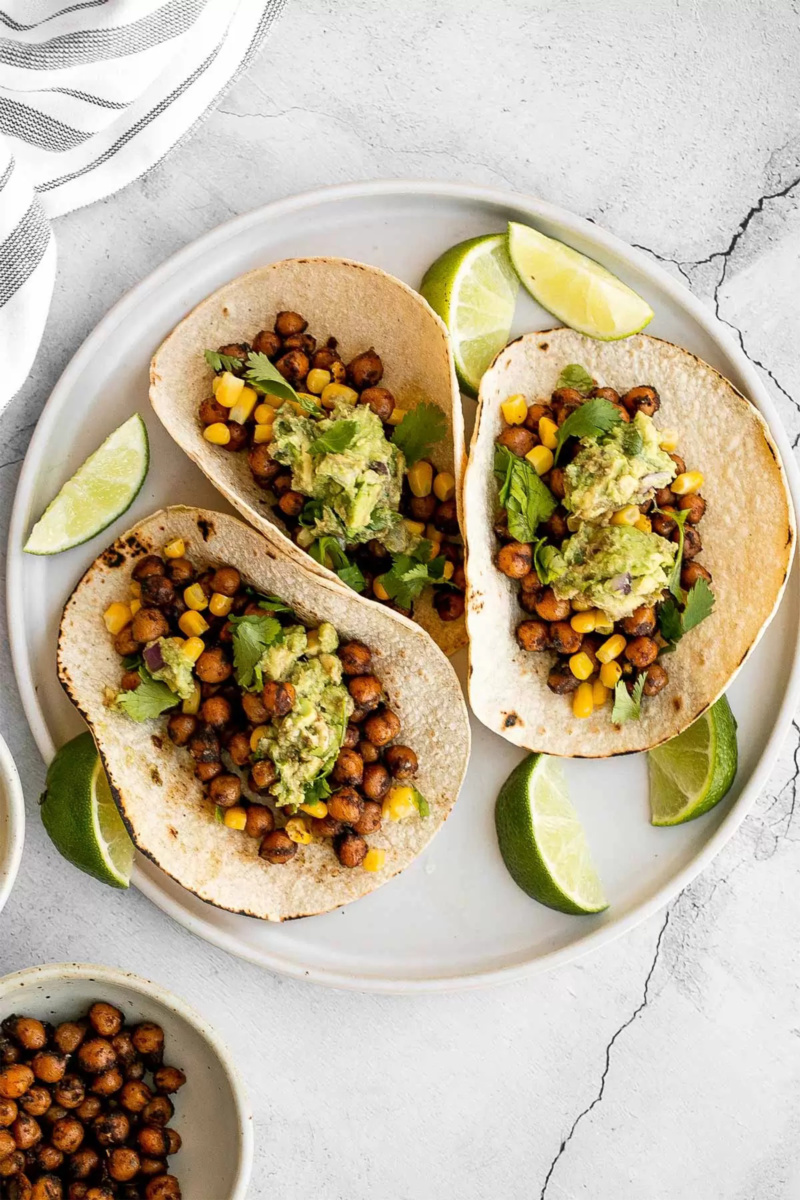 a plate of three chickpea tacos served with lime wedges
