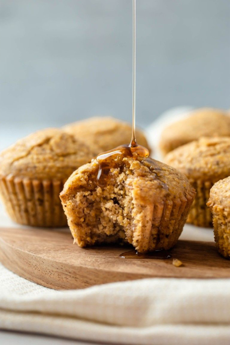 Maple syrup being drizzled on top of a vegan cornbread muffin with a bite taken out of it