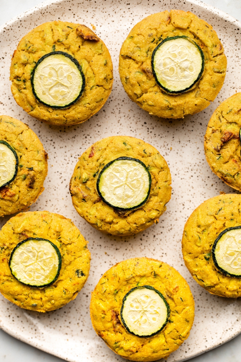 A plate of 8 savory zucchini muffins, each featuring a slice of zucchini on top