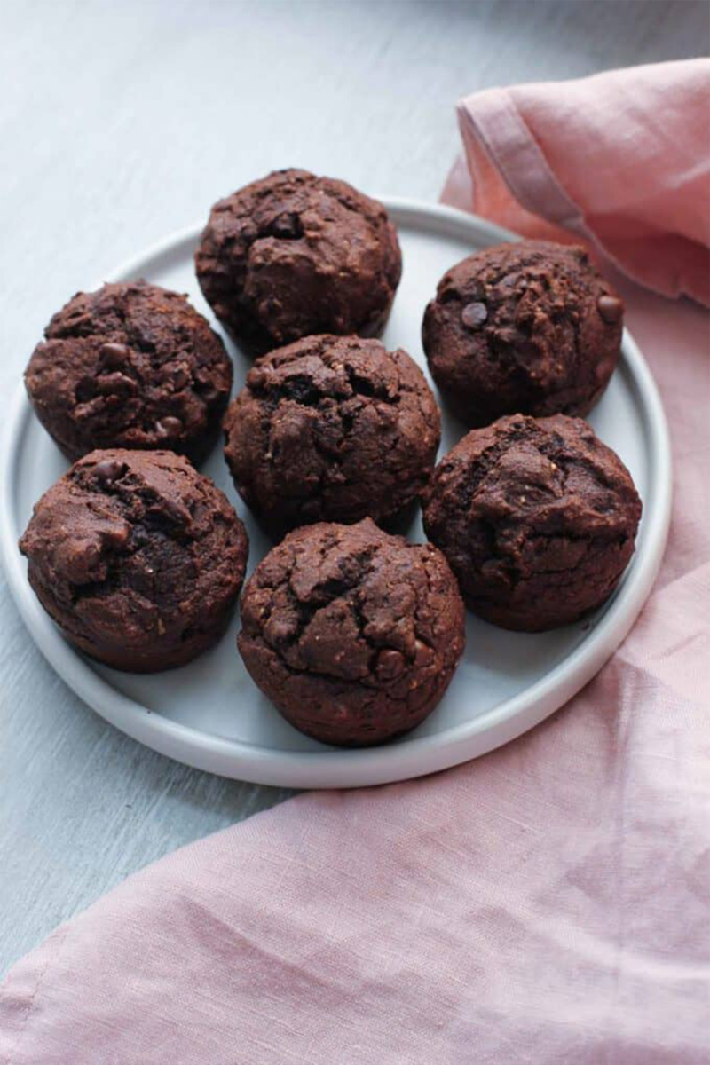 A plate of 7 chocolate muffins sits on a table with a pink dish towel