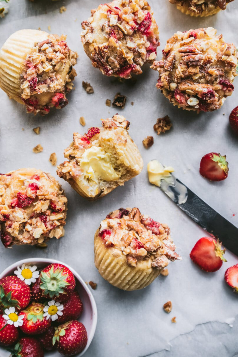 six strawberry streusel muffins are served next to a bowl of strawberries