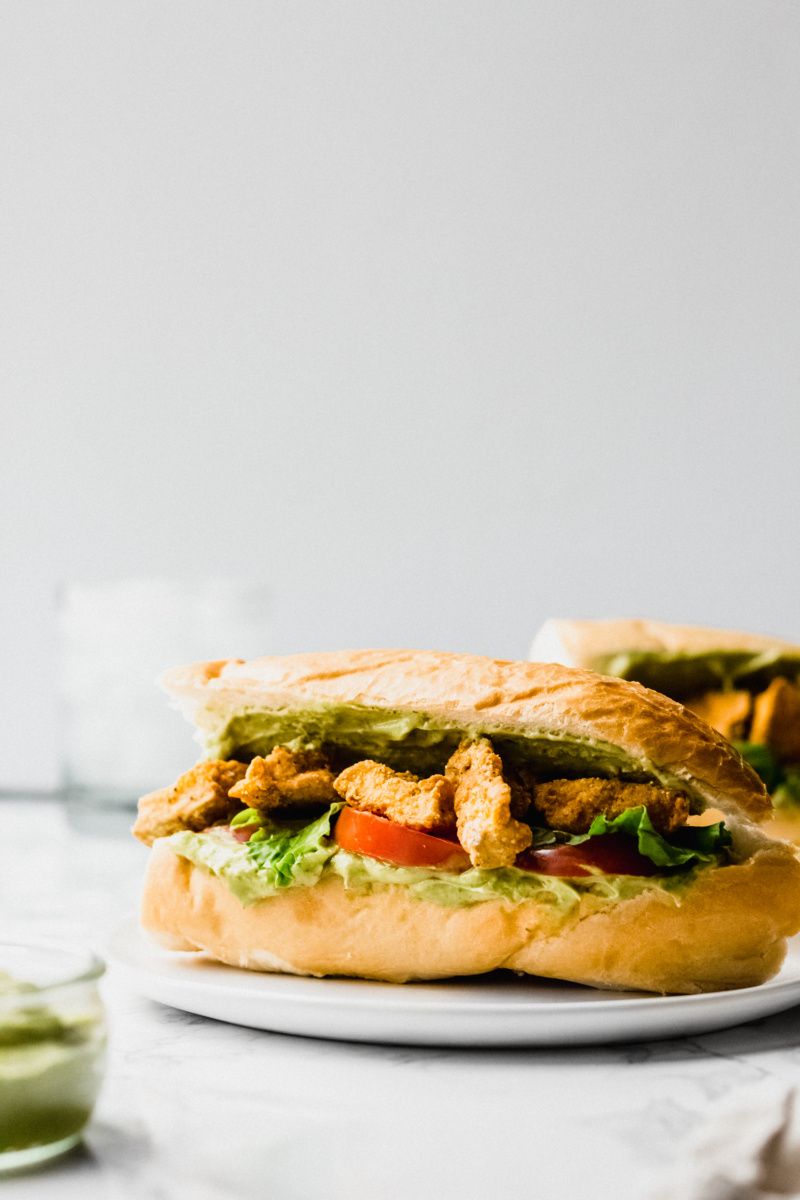 side view of a cajun po boy stuffed with fried tofu, tomatoes, and lettuce