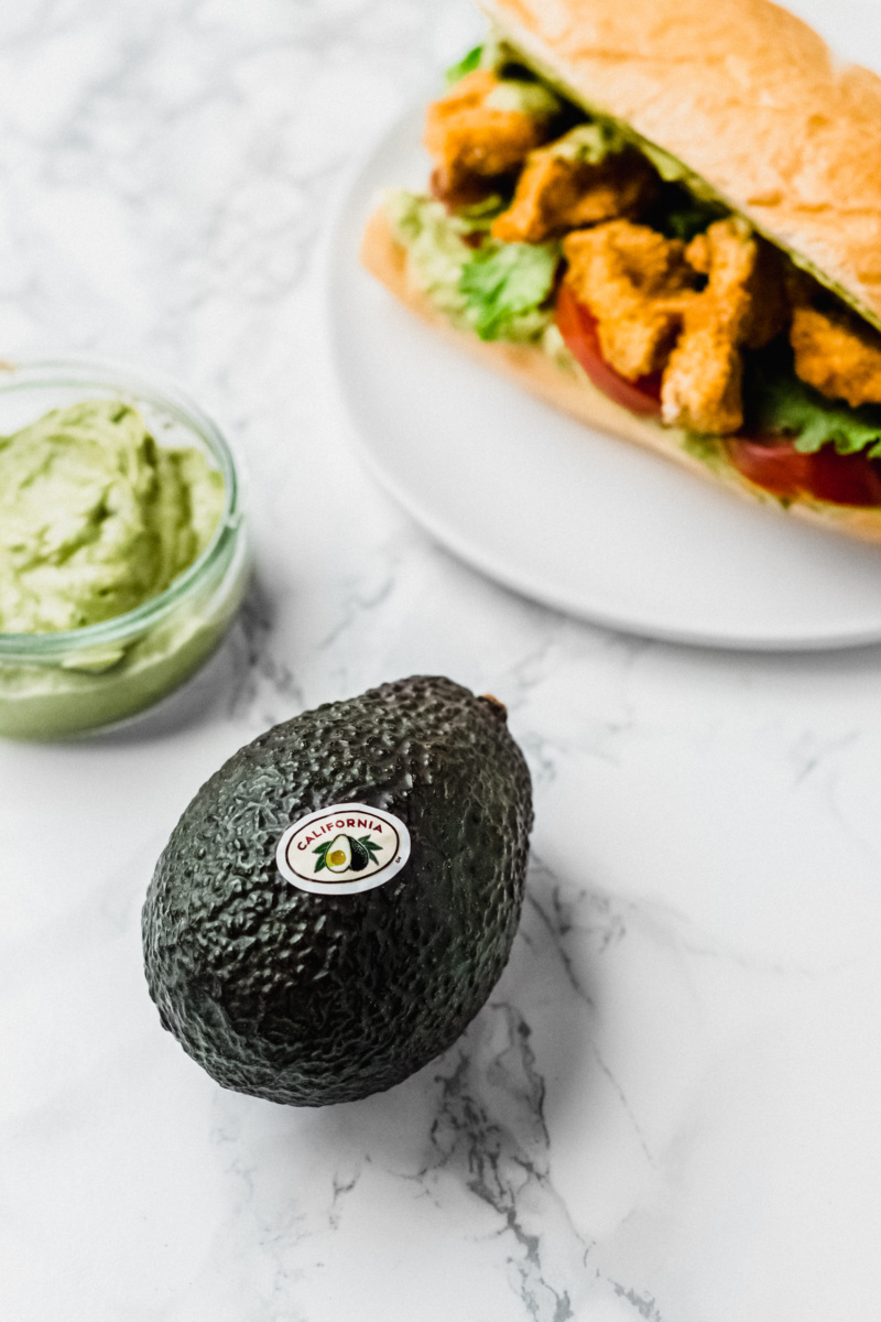 close up of an avocado next to a sandwich with fried tofu