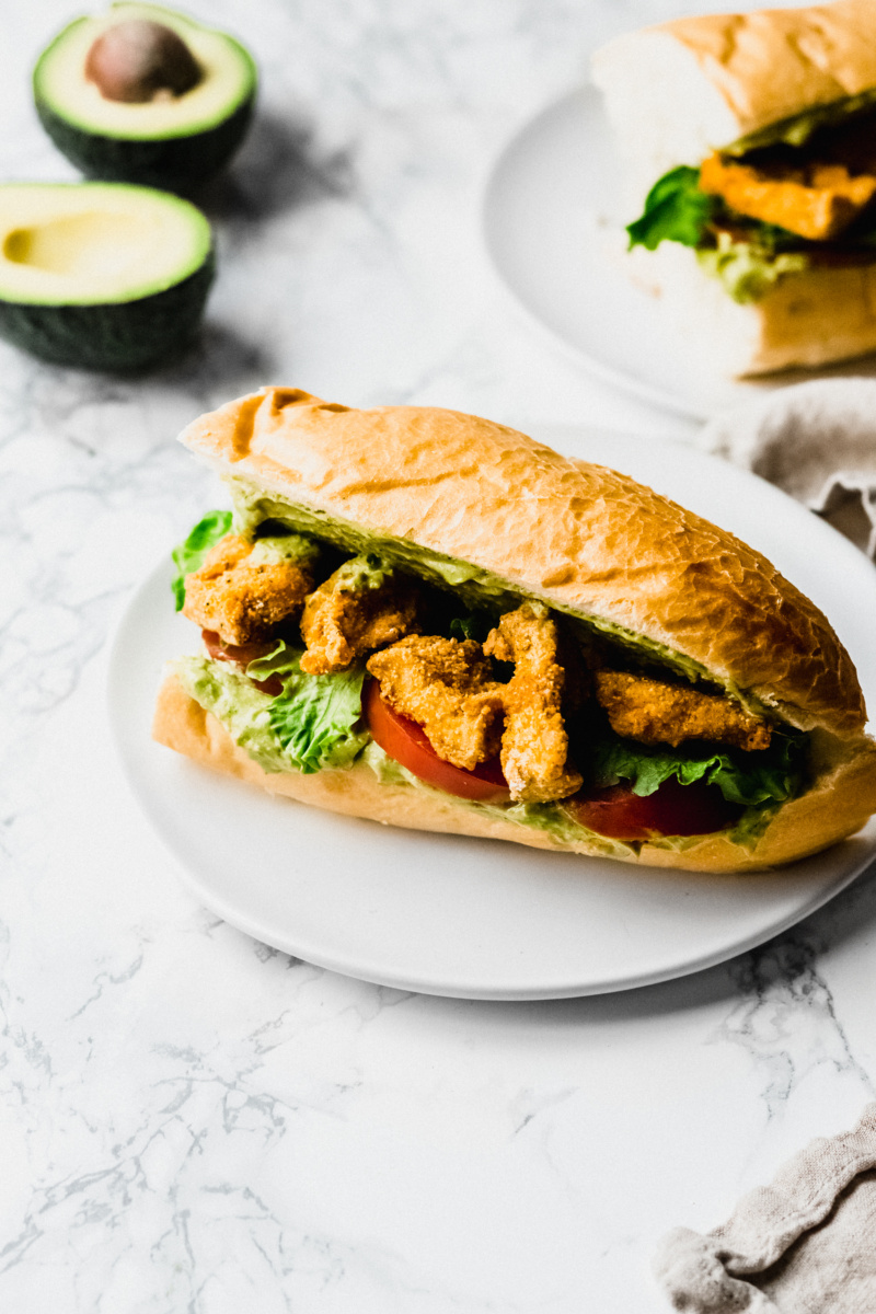 overhead view of a sandwich made with french bread, breaded tofu, avocado sauce, tomatoes, and lettuce