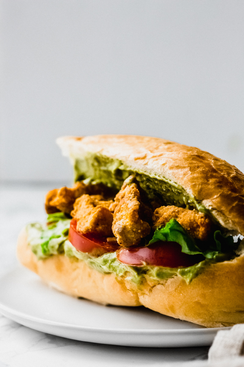 close up of fried tofu po boy on a loaf of white bread with tomatoes and lettuce