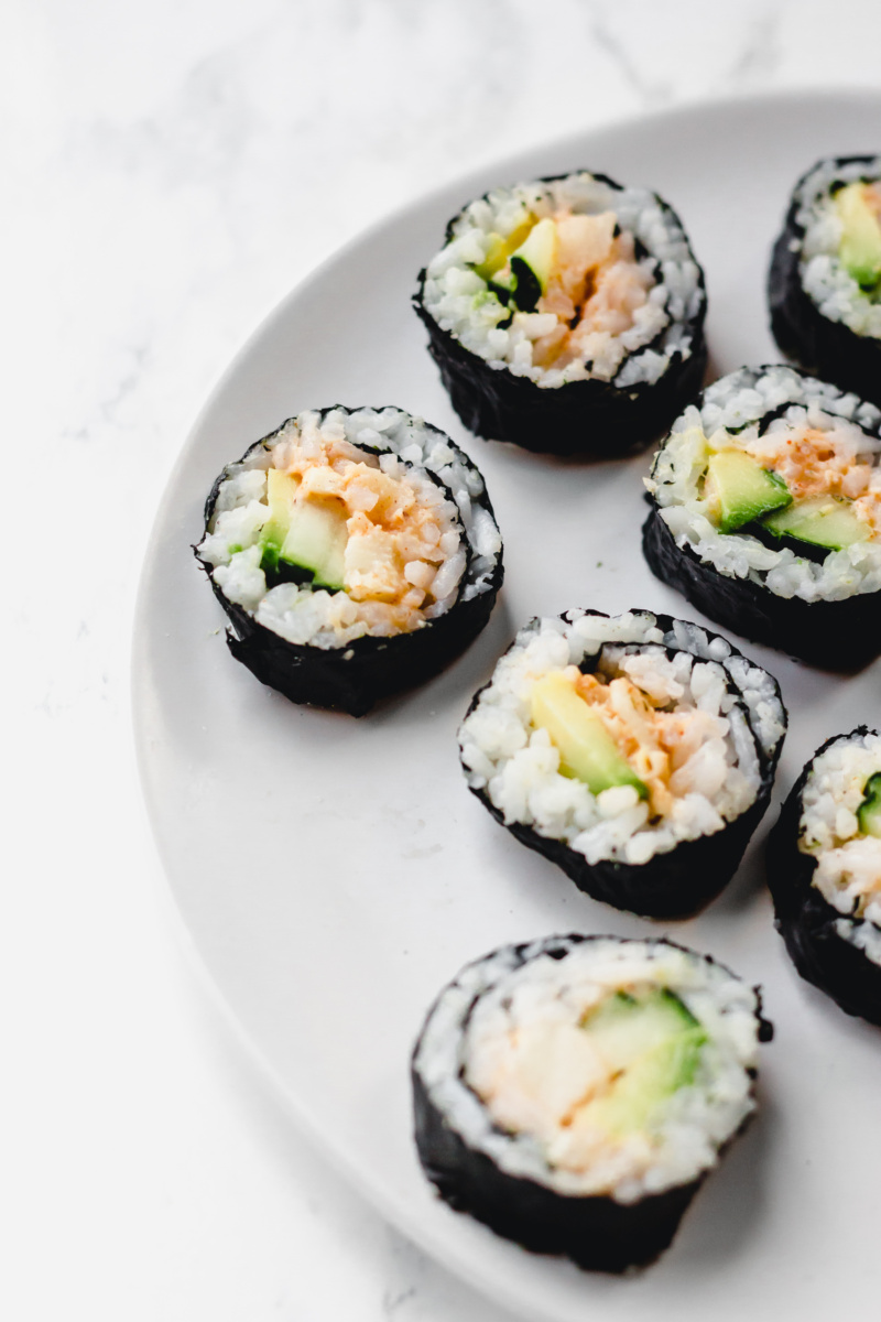 a close up of a plate of vegan sushi cut into slices. The sushi is fulled with avocado, cucumber and hearts of palm