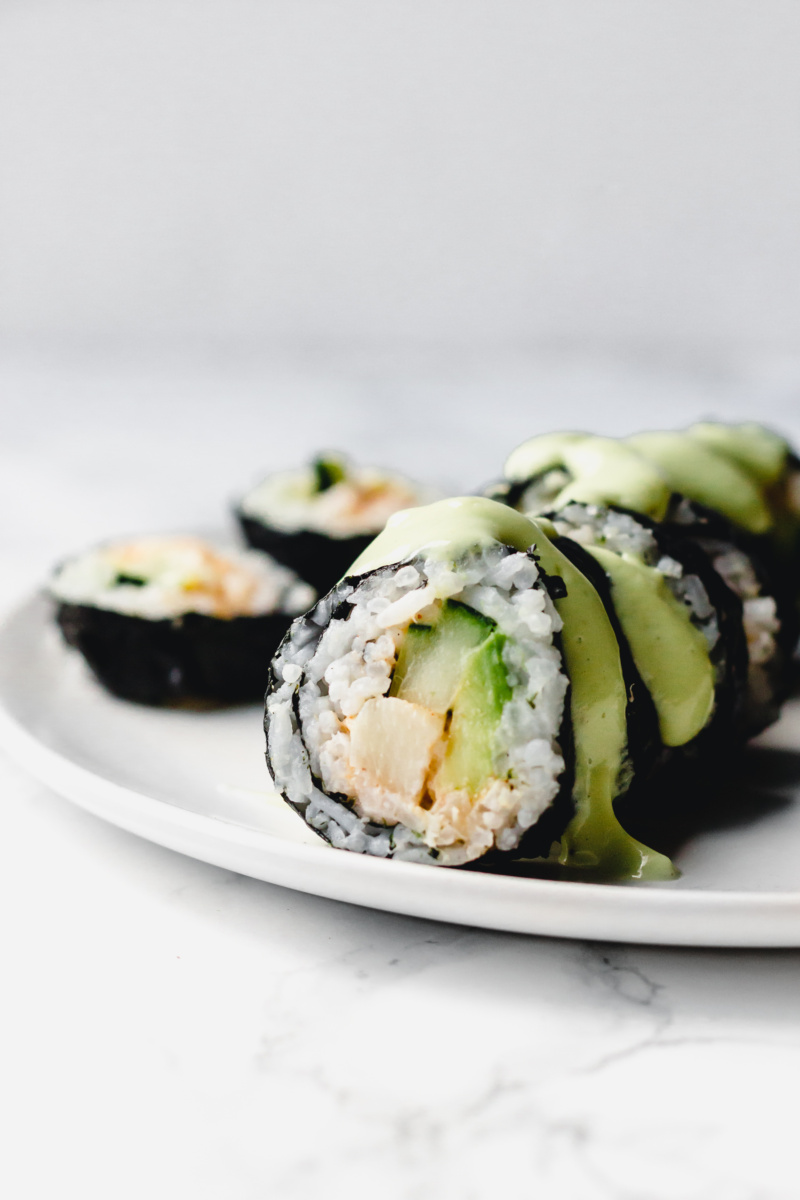 a close up of a vegan california roll, cut into slices and served with a drizzle of wasabi avocado sauce