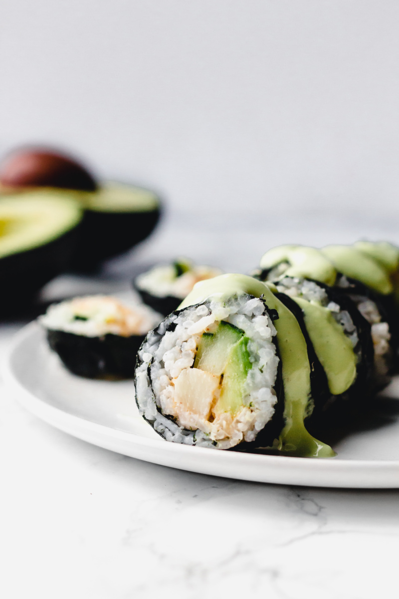 a vegan California roll filled with avocado, cucumber and hearts of palm topped with a wasabi avocado sauce