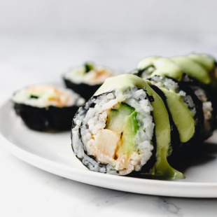 a close up of a vegan sushi roll filled with hearts of palm, avocado and cucumber and topped off with a drizzle of avocado wasabi sauce