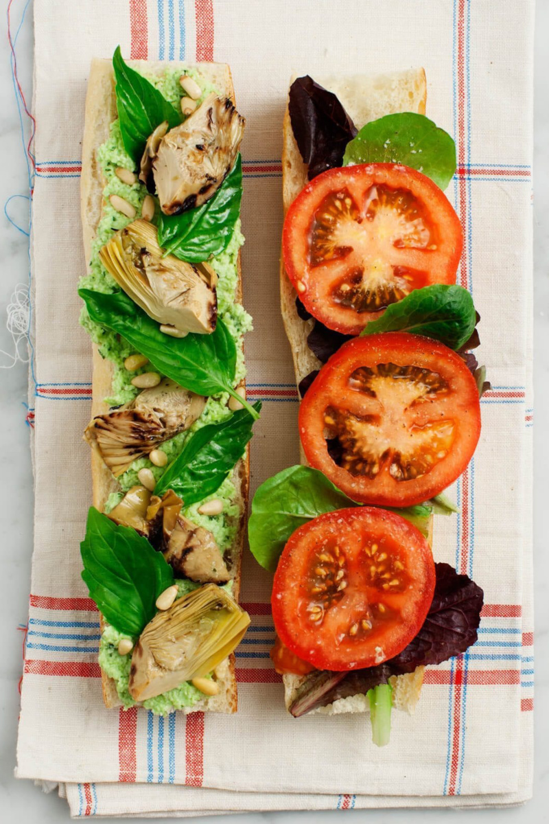 a large vegan sub sandwich with sliced tomatoes, basil, pesto and artichokes