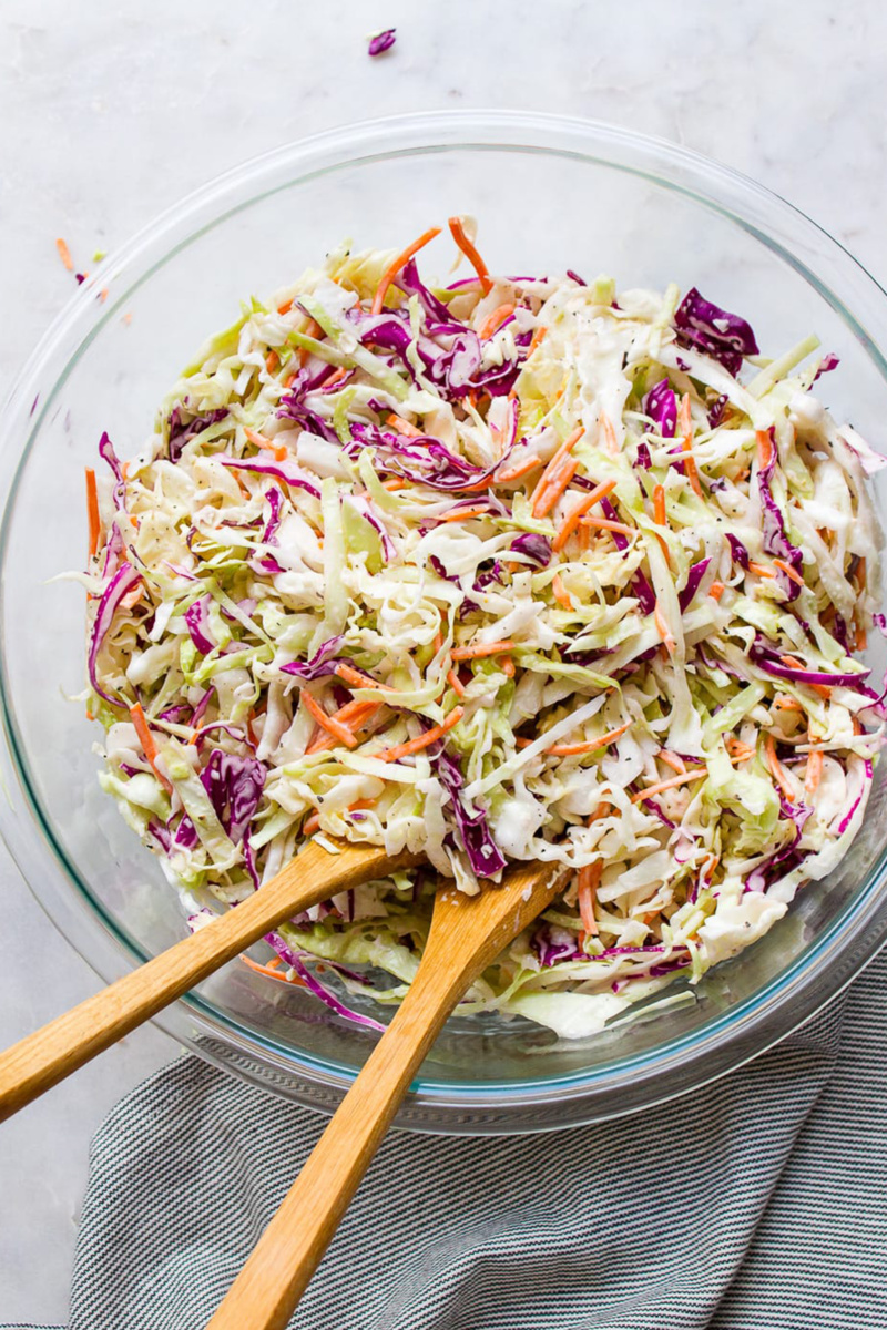 a large bowl of vegan coleslaw with wooden serving utensils