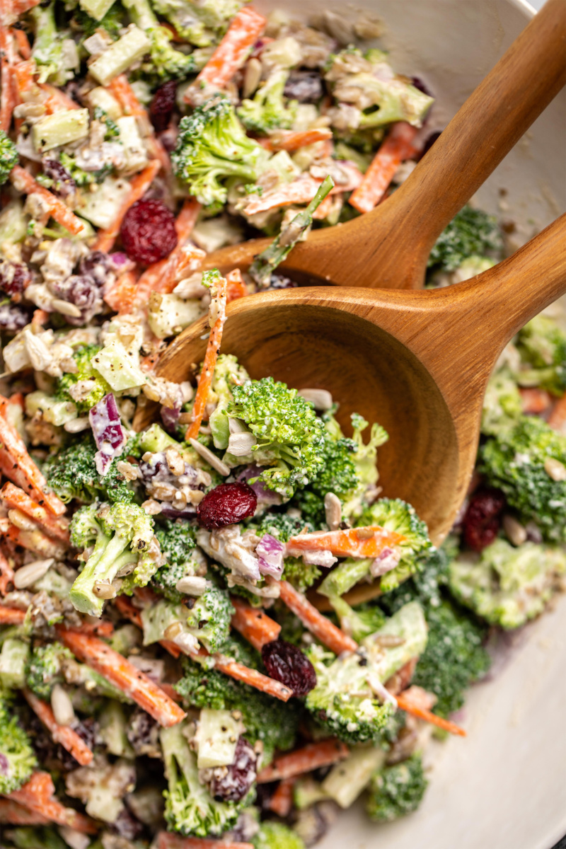 vegan broccoli salad being tossed with wooden serving spoons