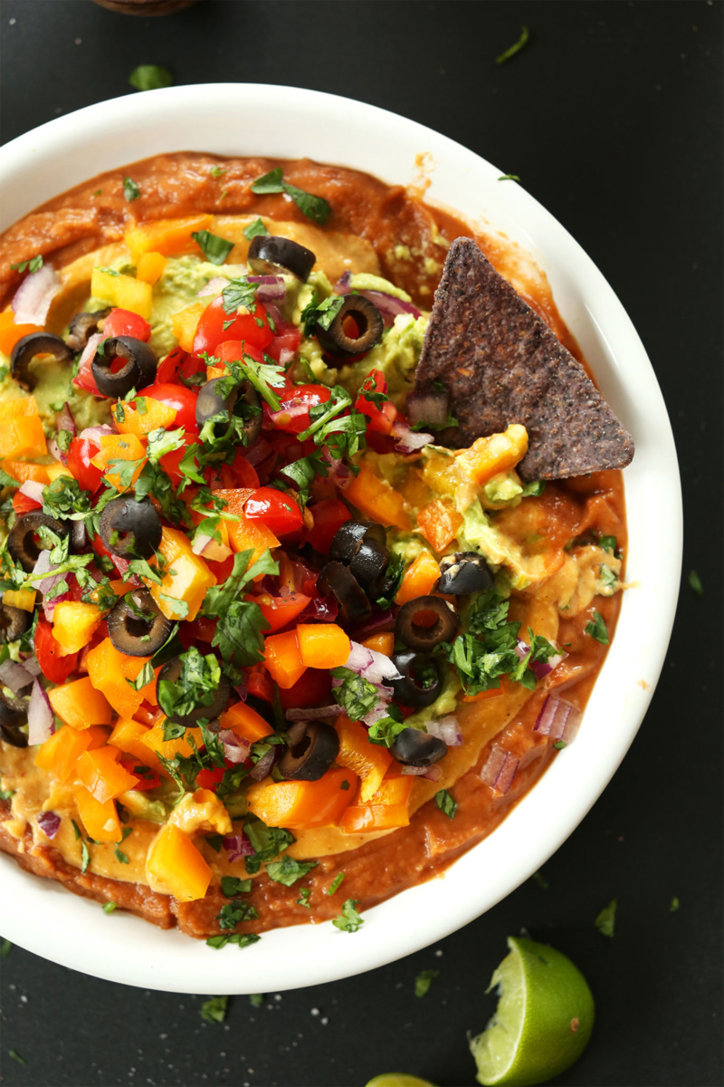 vegan 7 layer dip topped with chopped tomatoes, cilantro and black olives
