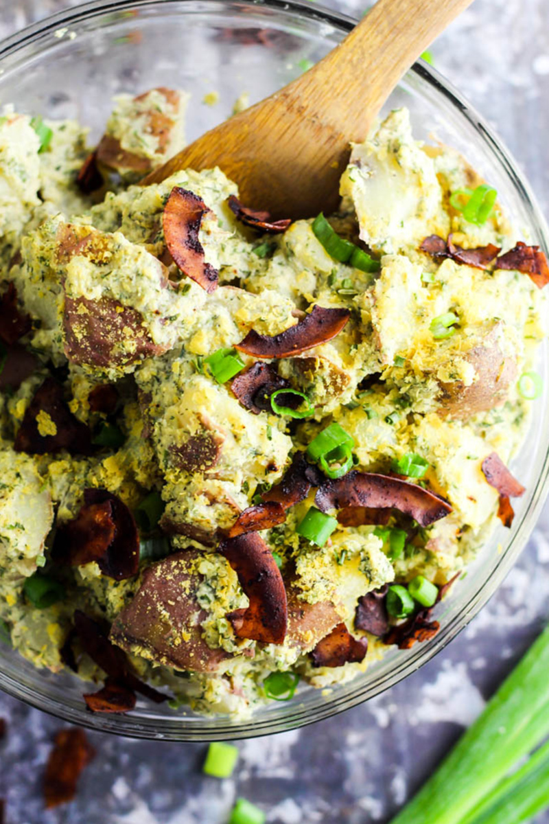 a large serving bowl of vegan potato salad topped with chopped green onion and coconut bacon