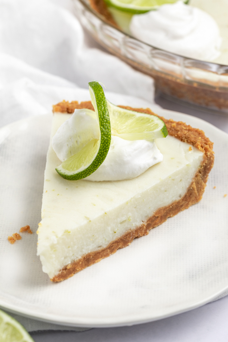 a slice of vegan key lime pie topped with whipped cream and a slide of fresh lime