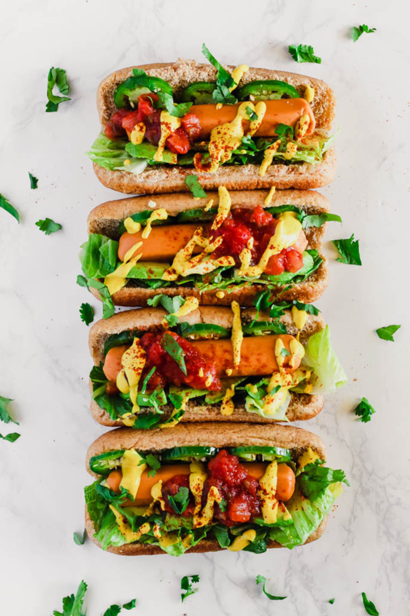 a lineup of four veggie dogs topped with lettuce, mustard, ketchup, jalapenos and salsa 