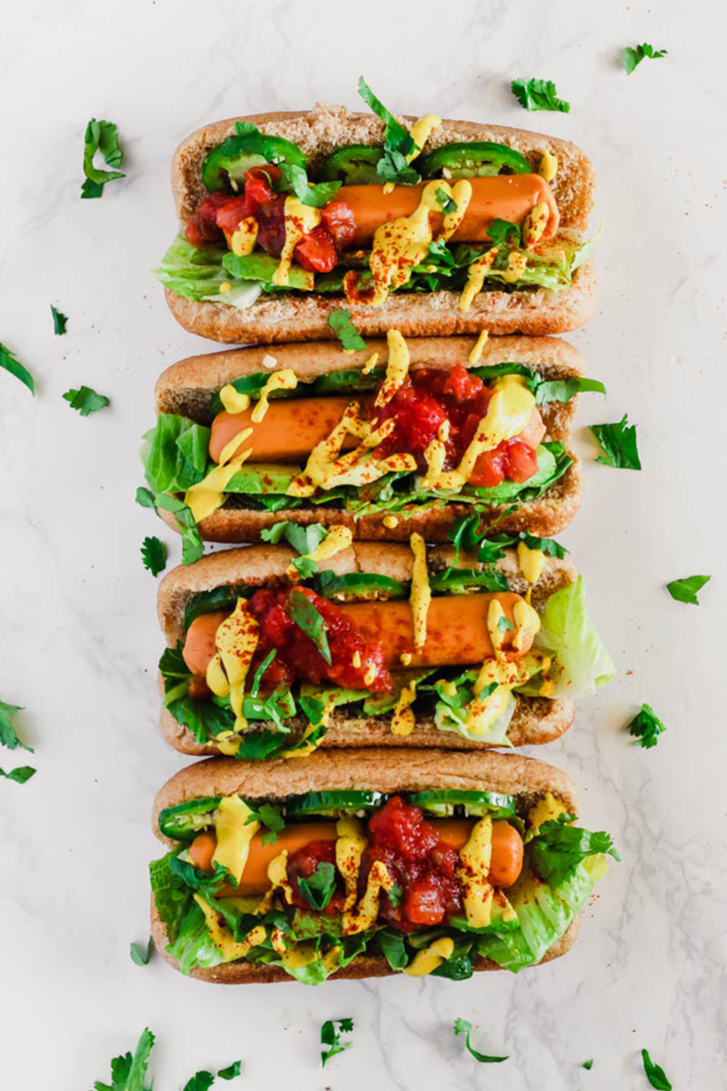 a lineup of four veggie dogs topped with lettuce, mustard, ketchup, jalapenos and salsa 