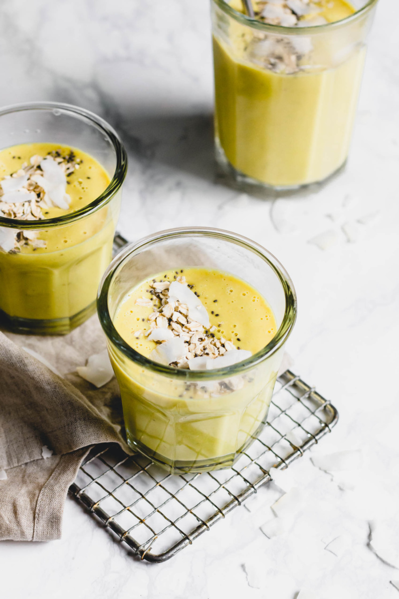 three glasses of a pina colada smoothie topped with coconut flakes