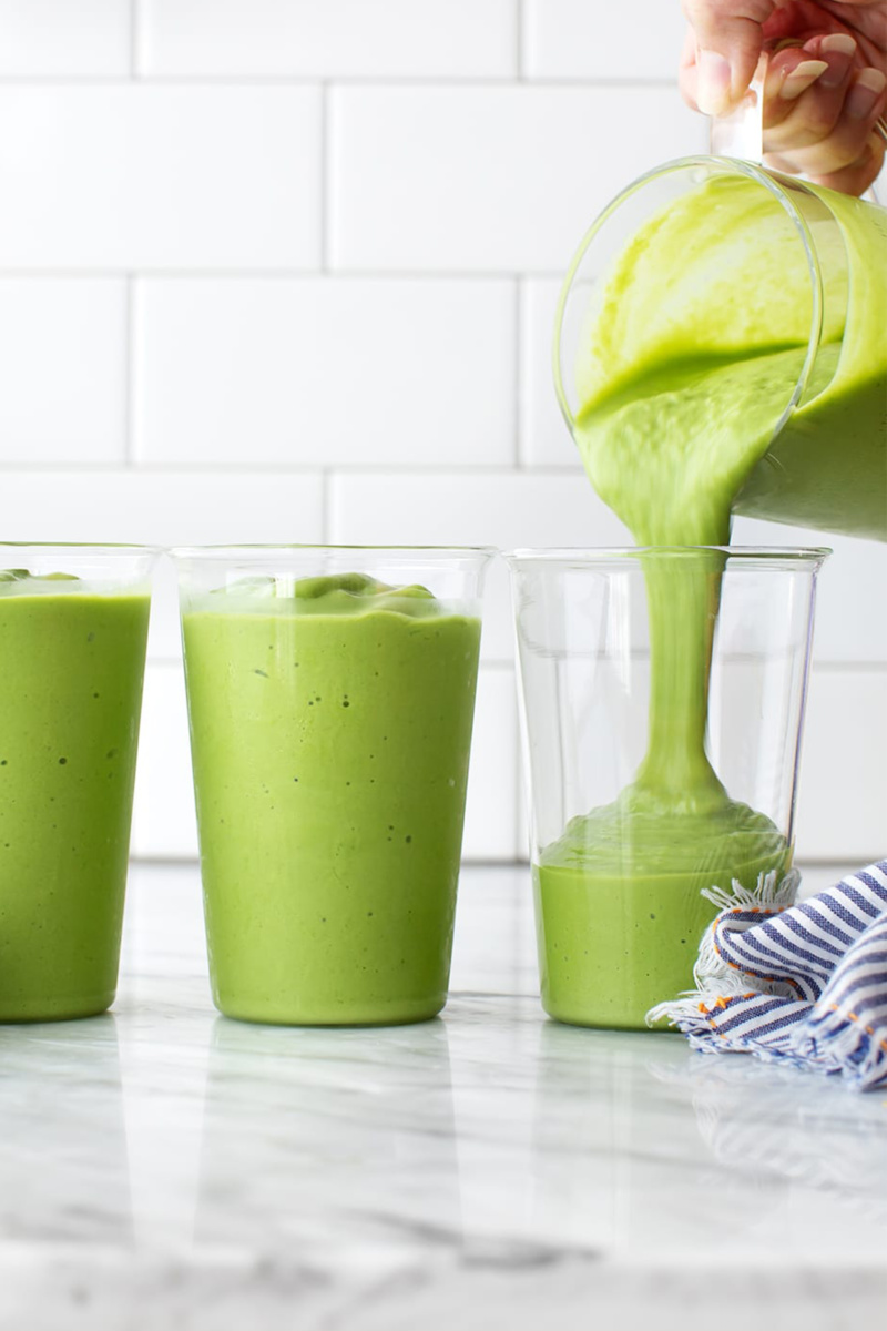 a blender pouring a green smoothie into a glass