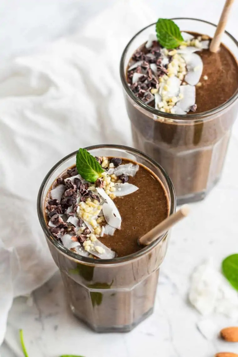 two chocolate smoothies topped with mint, chocolate chips and coconut flakes